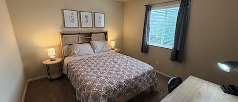Une chambre à coucher avec un lit, des tables de chevet, un bureau et une fenêtre avec des rideaux.