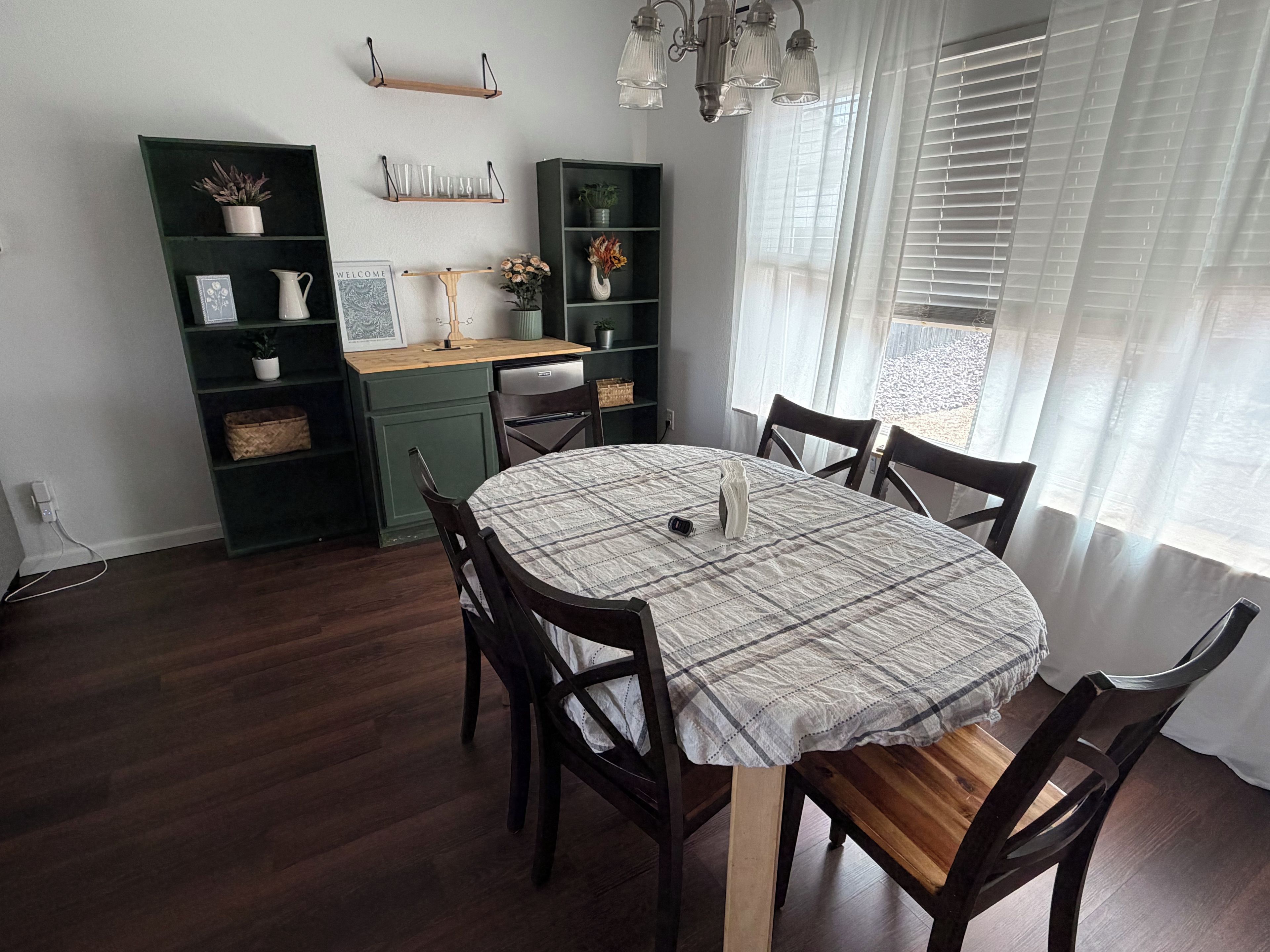 A dining area with a round table, chairs, a green cabinet, and a window with blinds.