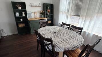 A dining area with a round table, chairs, a green cabinet, and a window with blinds.
