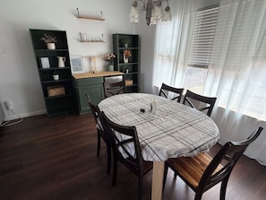 Un coin repas comprenant une table ronde, des chaises, un meuble vert et une fenêtre avec des stores.