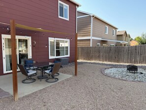 Un patio con mesa y sillas, una pérgola de madera y suelo de grava.