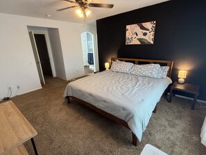 A bedroom with a bed, a ceiling fan, a nightstand, and a wall-mounted lamp.