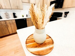 A kitchen with wooden cabinets, a white countertop, and a vase with dried plants on a wooden board. - Pool View Retreat, Modern 2BR Near Energy Corridor (Houston)