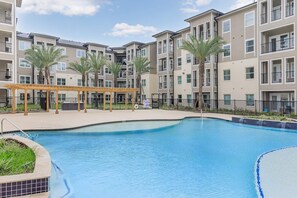 A residential building with a swimming pool, palm trees, and a covered patio area. - Pool View Retreat, Modern 2BR Near Energy Corridor (Houston)