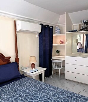 A bedroom with a bed, bedside table, lamp, chair, dresser, and a mirror. - Cozy Island Retreat - short walk to beach & shops! (Choc)