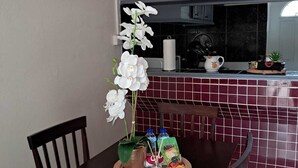 Ruokailutila, jossa on puinen pöytä, tuoleja, seinällä oleva kello ja taustalla keittiö.