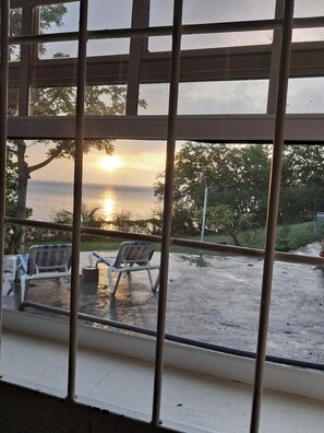 A view through a window with a metal grid, featuring a bench and a chair outside. - Cozy 1-bdrm with ocean views, short walk to beach & shops! (Choc)