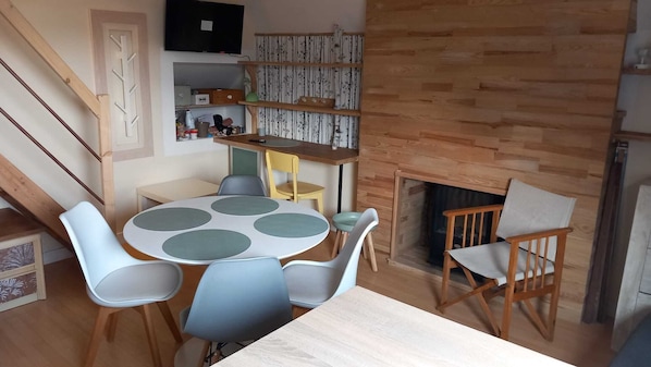 A dining area with a round table, chairs, a bookshelf, and a fireplace.