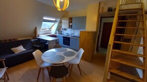 A compact living space with a dining area, kitchenette, and a loft bedroom accessible by a wooden ladder.