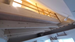 A room with a sloped ceiling, wooden beams, and a visible ductwork system.