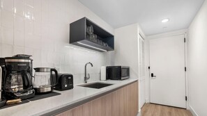 A modern kitchen with a coffee maker, toaster, microwave, and a shelf with glasses. - Downtown Studio Near Kaseya & Brickell |Pool & Gym (Miami)