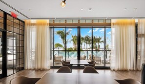 A modern hotel room with a large balcony, a dining area with a table and chairs, and a view of palm trees and a building across the water. - Downtown Studio Near Kaseya & Brickell |Pool & Gym (Miami)