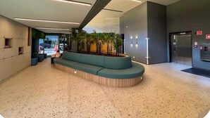 Un hall d’entrée moderne doté d’un espace salon aux lignes courbes, d’un comptoir d’accueil et d’un ascenseur.