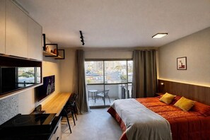 Ein Hotelzimmer mit Bett, Schreibtisch, Stuhl, Fernseher, einem Fenster mit Blick auf Gebäude und einem Balkon.