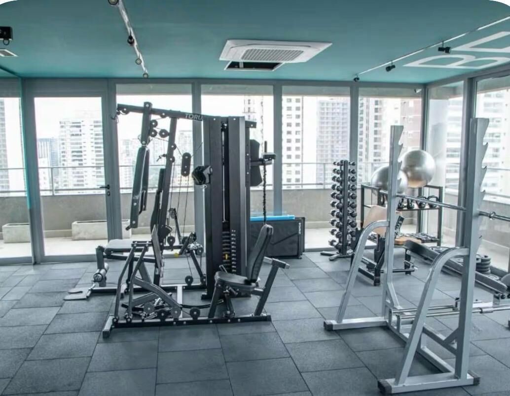 Une salle de sport équipée de divers appareils d’exercice, dotée de grandes fenêtres et offrant une vue sur les immeubles de grande hauteur.