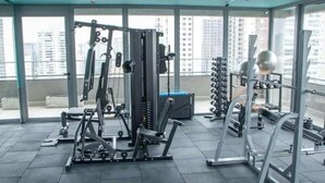 Une salle de sport équipée de divers appareils d’exercice, dotée de grandes fenêtres et offrant une vue sur les immeubles de grande hauteur.
