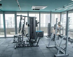 Ein Fitnessstudio mit unterschiedlichen Trainingsgeräten, großen Fenstern und Blick auf Hochhäuser.