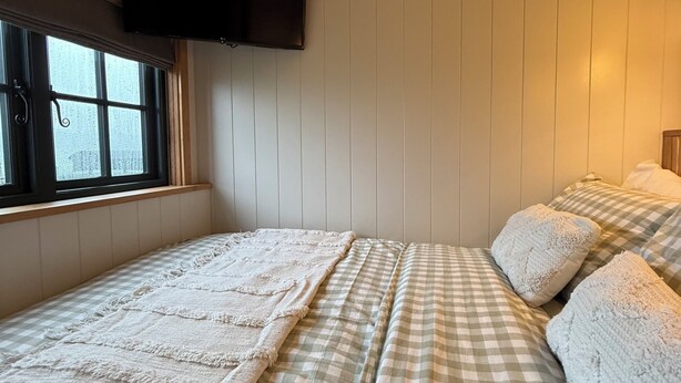 A room with a bed, a television mounted on the wall, and a window.