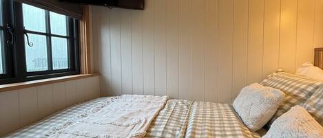 Una habitación con una cama, un televisor montado en la pared y una ventana.