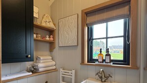 A bathroom with a white toilet, a sink with a brass faucet, a towel rack, and a window with a view of the outside.