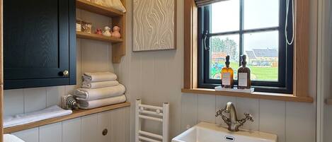A bathroom with a white toilet, a sink with a brass faucet, a towel rack, and a window with a view of the outside.