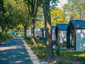 A row of small, single-story cabins with outdoor seating, surrounded by trees and a gravel path. - Nature Chalet Near Efteling (Kaatsheuvel)