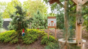 A garden area with a wooden signpost, a gnome statue, and a wooden structure. - Nature Chalet Near Efteling (Kaatsheuvel)