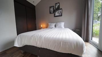 A modern bedroom with a large bed, a dark wardrobe, and a bedside table.
