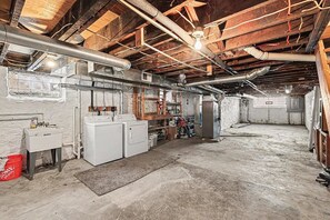 Ein Kellerraum mit freiliegenden Holzbalken, einer Waschmaschine, einem Spülbecken und einem roten Eimer.