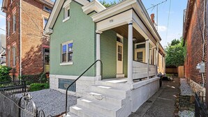 Uma casa de dois andares com fachada verde, varanda com grades brancas e exterior de tijolos.