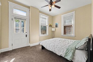 Ein Schlafzimmer mit einem Bett, einem Deckenventilator und zwei Fenstern mit Jalousien.