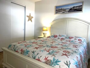 Ein Schlafzimmer mit einem Bett, einem Nachttisch, einer Lampe, einer Meeressterne-Dekoration und einem gerahmten Bild an der Wand.