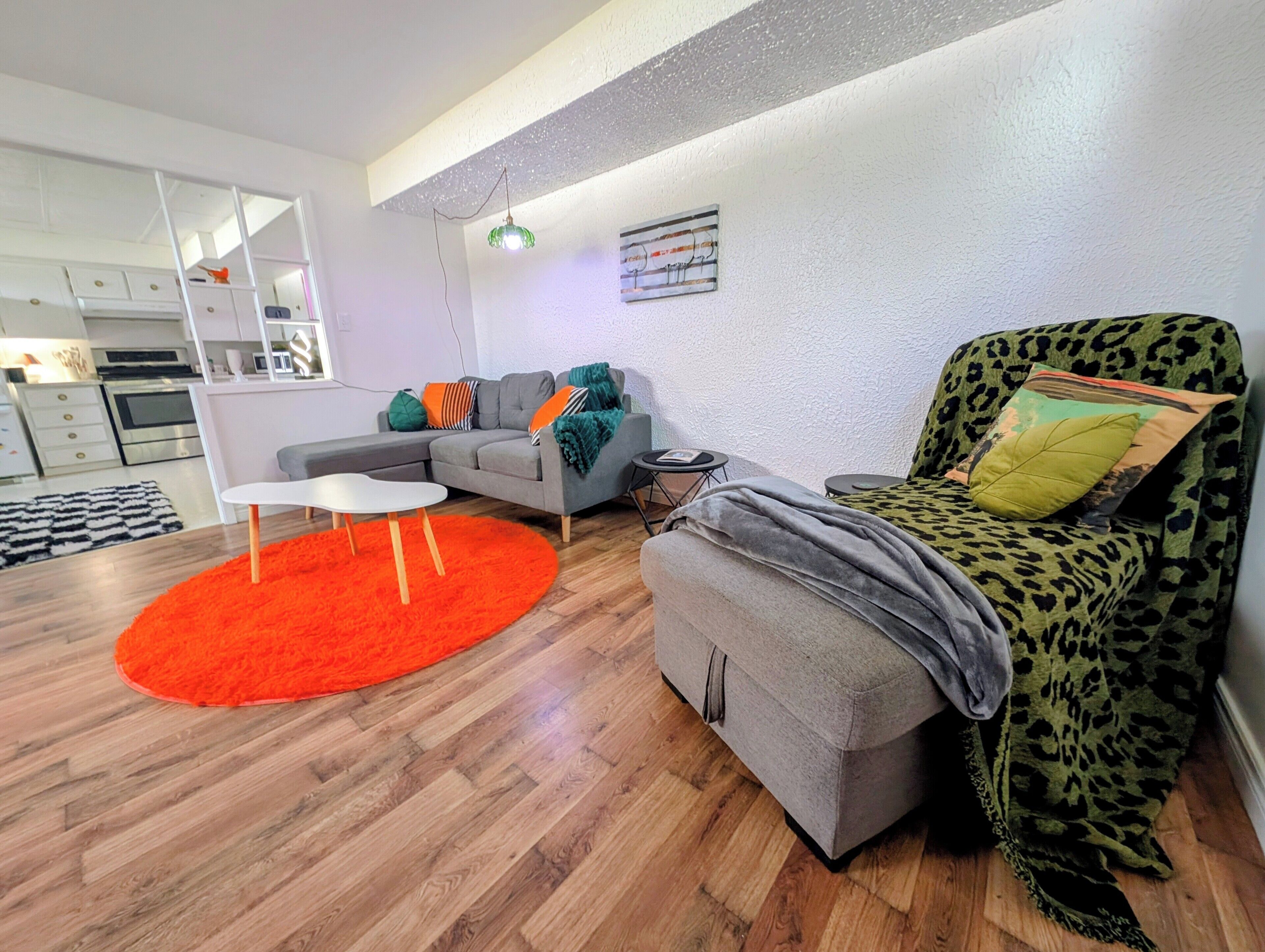 Een moderne woonkamer met een grijze bank, een fauteuil met luipaardprint, een rood vloerkleed en een klein witte tafeltje.