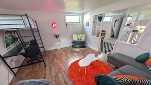 Un soggiorno moderno con un letto a castello, un divano grigio con cuscini colorati, un tappeto rosso e un piccolo tavolino bianco.
