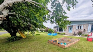 Un immobile residenziale con un prato curato, un'area giochi attrezzata e un grande albero.