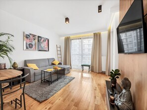 A modern living room with a grey sofa, a coffee table, and a dining area with a wooden table and chairs. - Comfortable Apartment in Warsaw for 4 Guests (Warsaw)