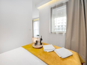 A hotel room with a bed, a small table with a bottle and glasses, and a window with curtains. - Comfortable Apartment in Warsaw for 4 Guests (Warsaw)