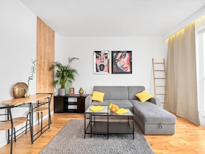 Ein modernes Wohnzimmer mit grauem Sofa, Couchtisch, Holzsideboard und einem Blumentopf.
