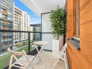 Ein Balkon mit Blick auf moderne Gebäude, einer Topfpflanze und zwei weiße Klappstühle.