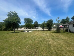 A grassy outdoor area with trees, a fenced parking lot, and a building with a covered patio. - Blue Anchor Beach House (Middle Township)