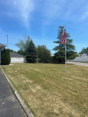 A grassy area with a flagpole, a white picket fence, and a building with a dark roof. - Blue Anchor Beach House (Middle Township)