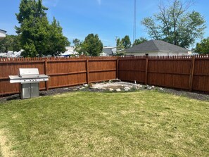 A backyard with a wooden fence, a barbecue grill, and a small pond. - Blue Anchor Beach House (Middle Township)