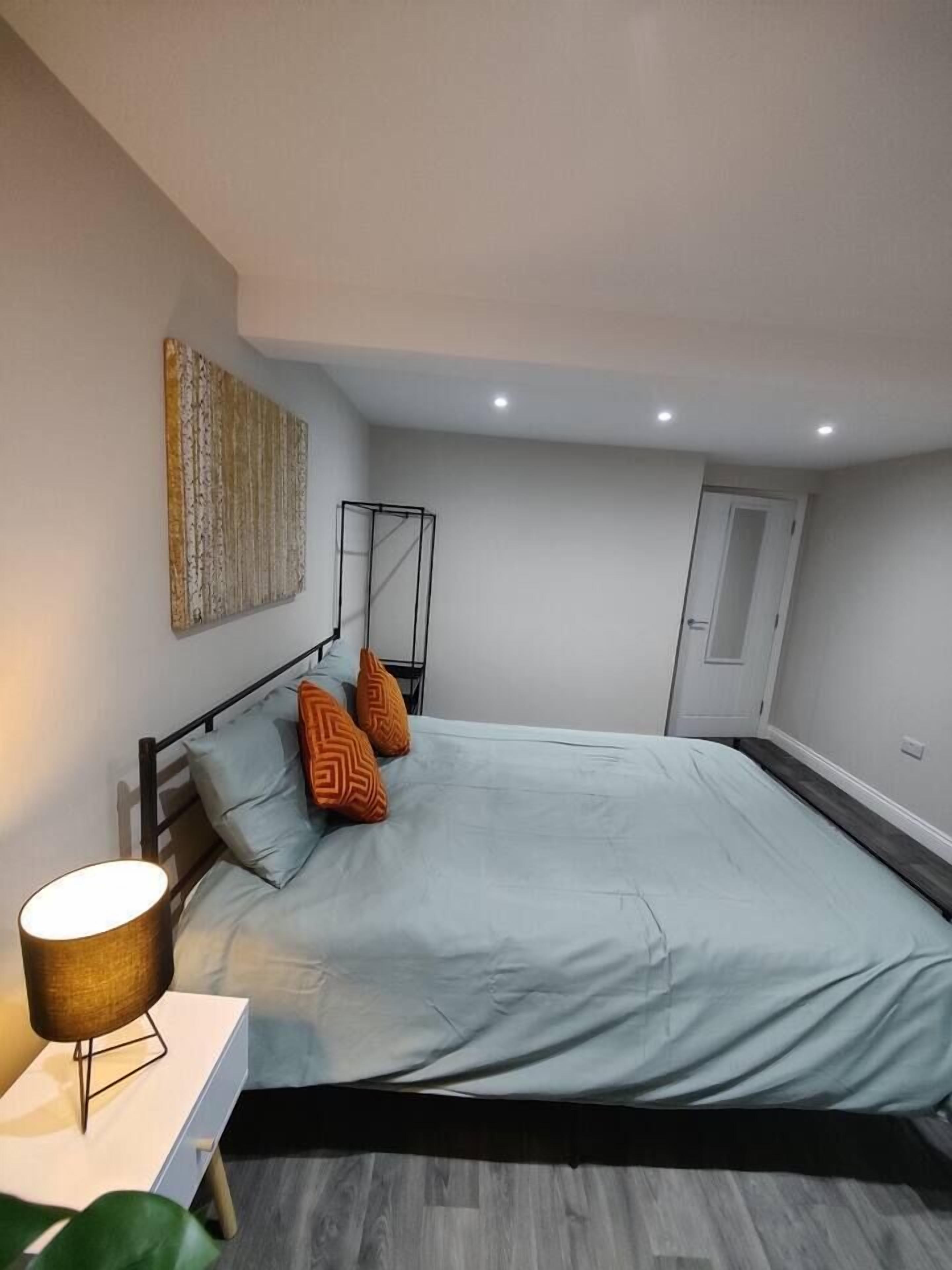 A bedroom with a bed, a bedside table, a lamp, and a wall-mounted artwork.