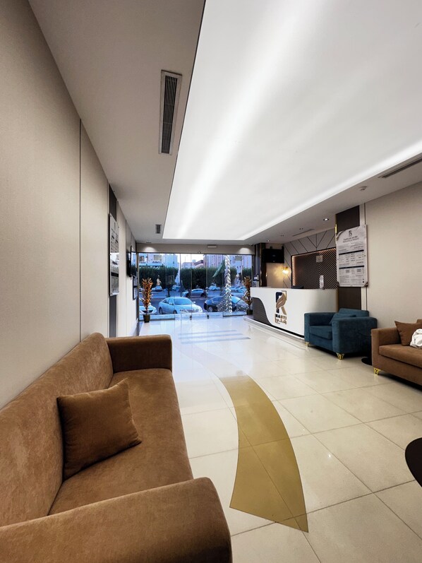 A modern lobby with a reception desk, seating area, and a view of the street outside.