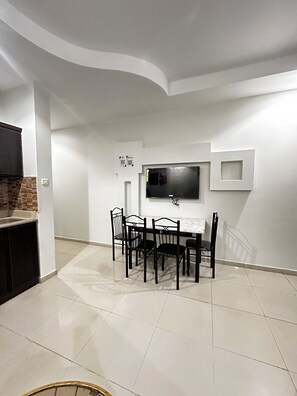 Una sala de estar moderna con comedor, un televisor de pantalla plana en la pared y una cocina con armarios oscuros.