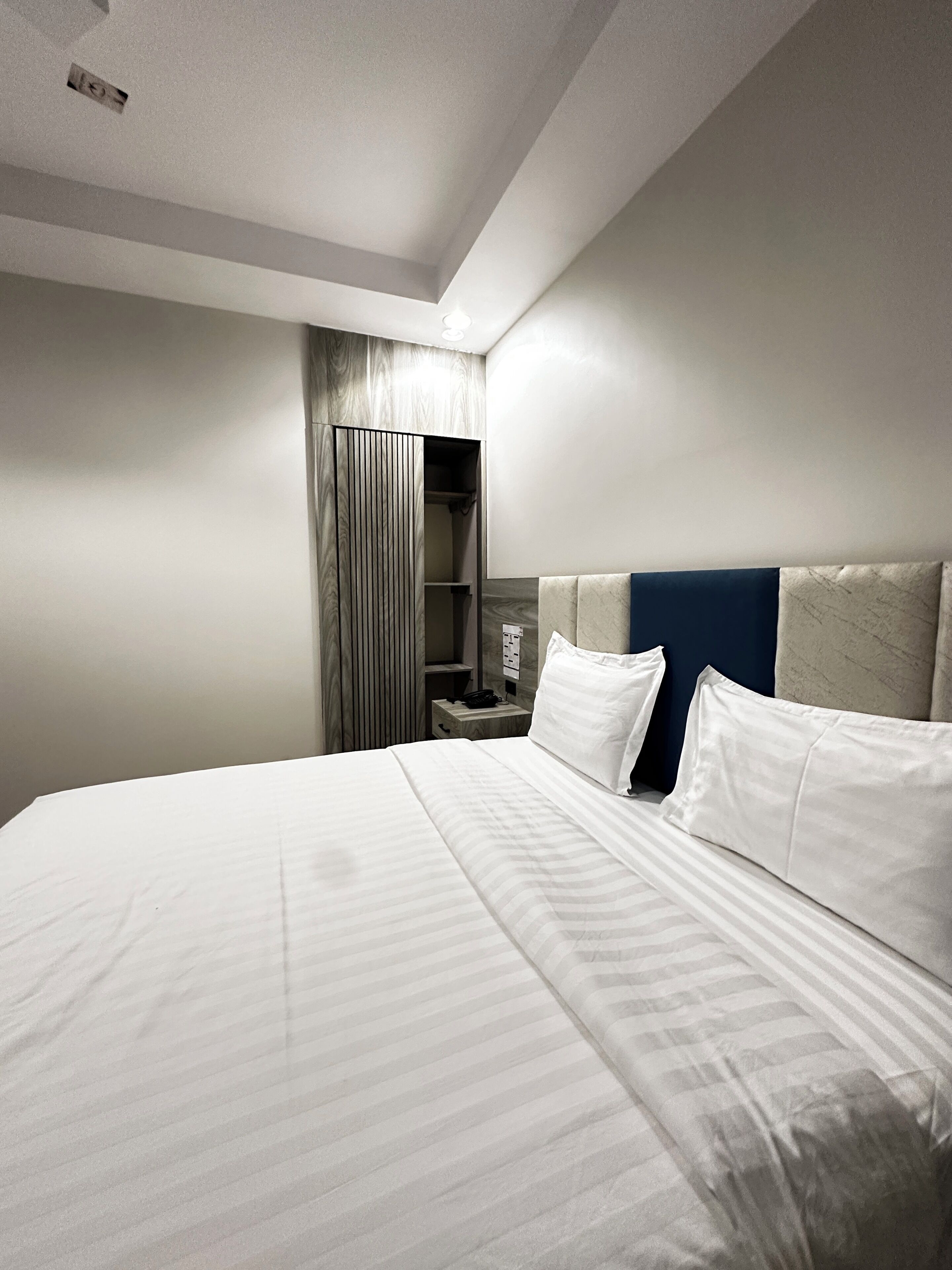 A hotel room with a bed, a nightstand, a wardrobe, and a headboard.
