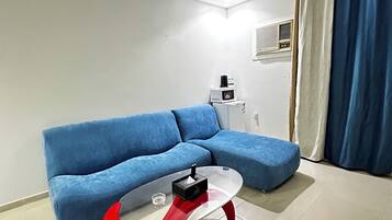 Ein Wohnzimmer mit einem blauen Sofa, einem roten und transparenten Couchtisch und einer weißen Klimaanlage an der Wand.
