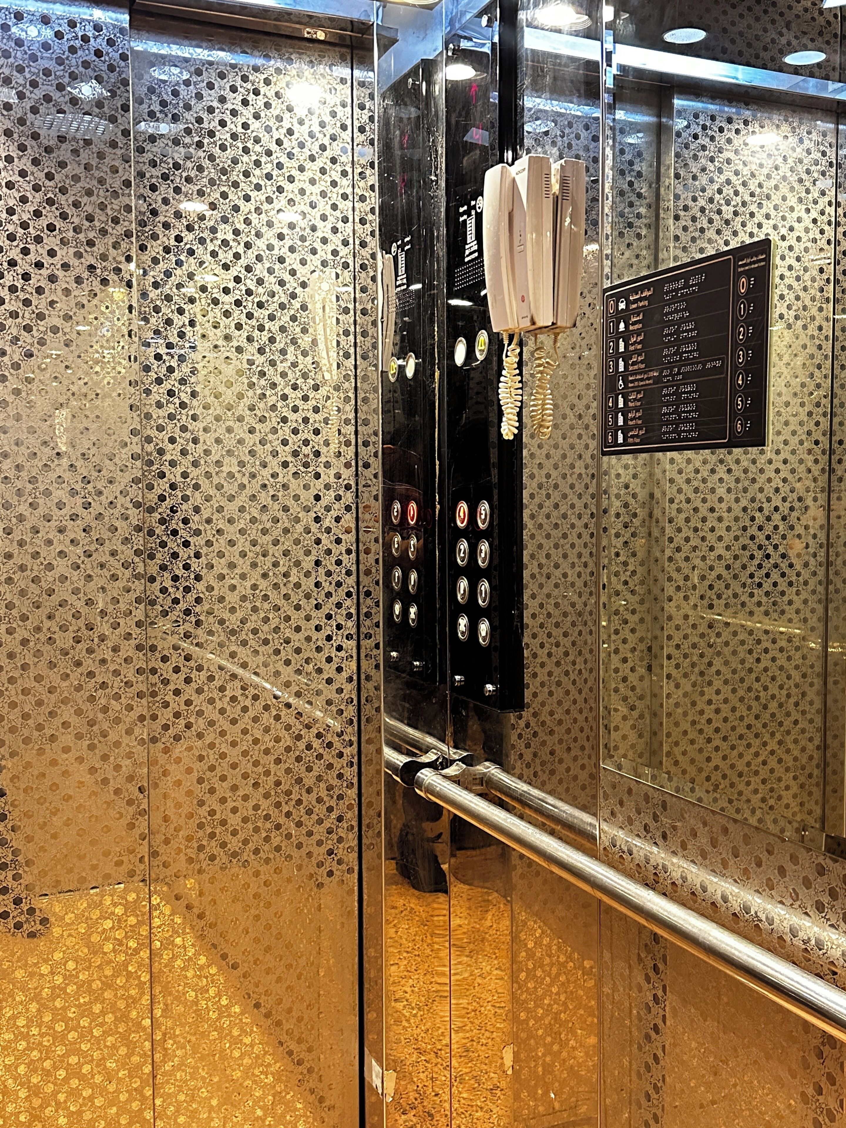 Um elevador com parede metálica texturizada e painel digital com números de andares.