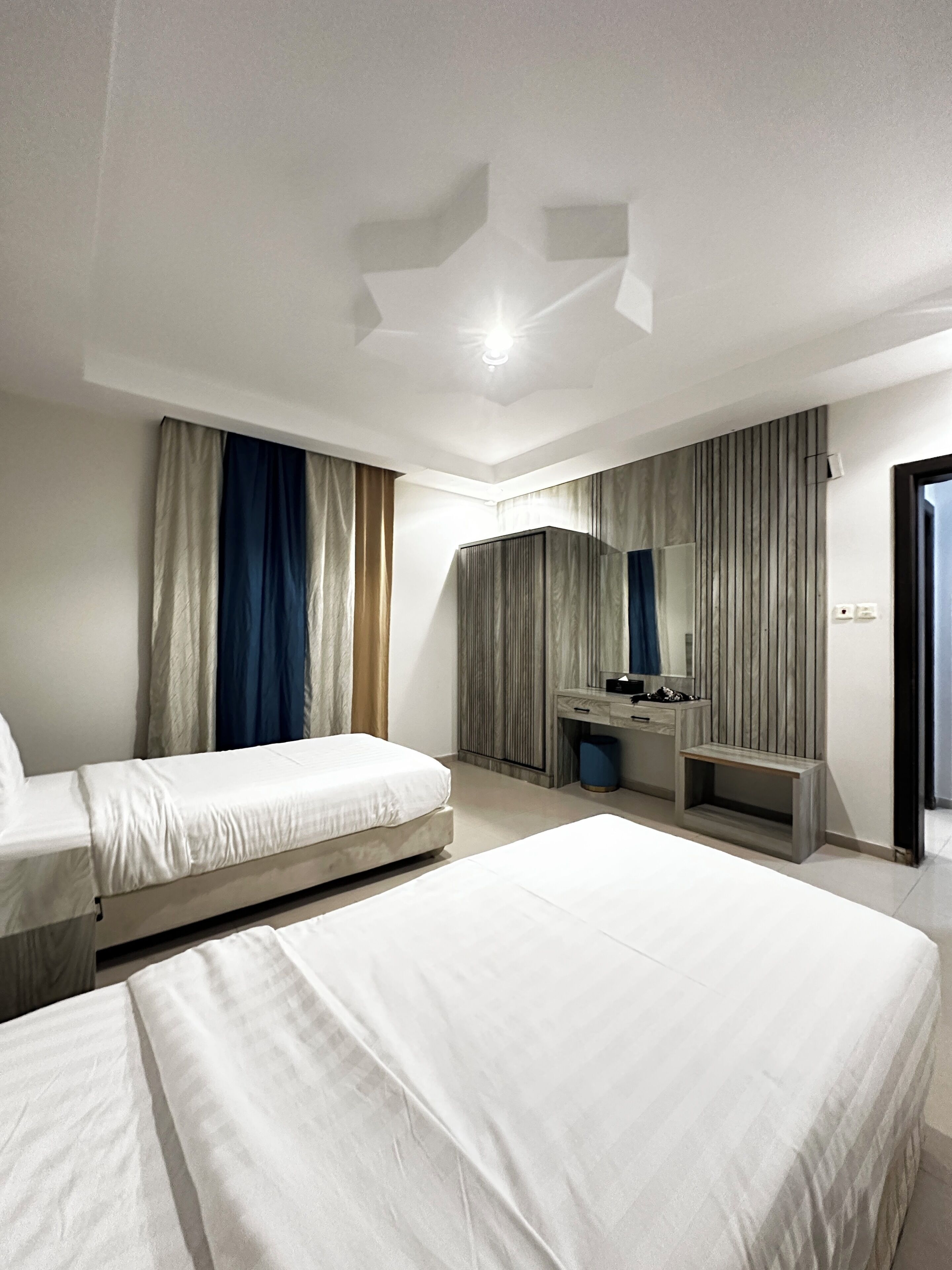 Une chambre d’hôtel avec deux lits, une coiffeuse avec un miroir et une grande fenêtre avec des rideaux.