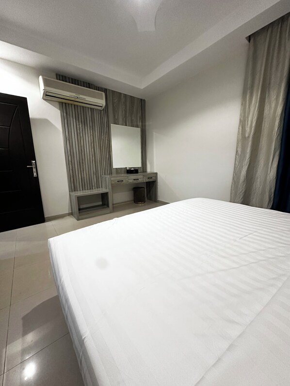 Habitación de hotel con una cama grande, un escritorio con silla, un espejo y un equipo de aire acondicionado.